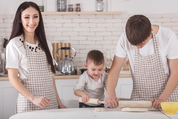 Entzückende Familie, die zusammen kocht. Junge Familie in der Küche beim Frühstück oder Abendessen. Mama, Papa und ihr kleines Kind bereiten Essen zu.