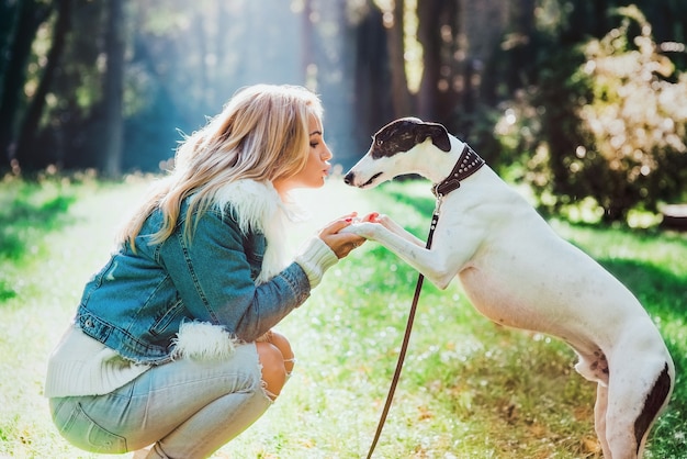 entzückende glückliche blonde Besitzerin mit ihrem weißen Whippet im Freien