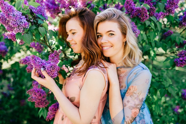 Entzückende glückliche fröhliche fabelhafte Zwillingsschwestern in verschiedenen schönen Sommerkleidern, die im Frühling blühenden Park aufwerfen.
