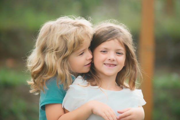 Foto entzückende glückliche kinder draußen am sommertag kleiner junge, der ein mädchen küsst schöner kleiner junge und mädchen haben