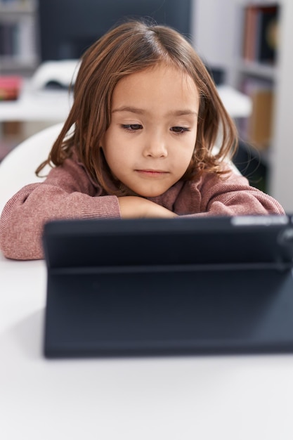 Entzückende hispanische Studentin mit Touchpad, die im Klassenzimmer auf dem Tisch sitzt