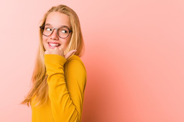 Entzückende Jugendlichfrau zeigt mit dem Daumenfinger weg, lachend und sorglos.