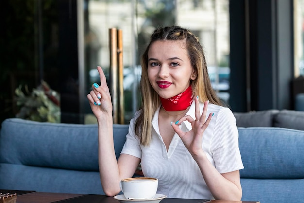 Entzückende junge Blondine sitzt im Restaurant und gestikuliert ok