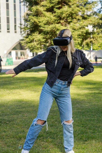 Entzückende junge Dame, die eine VR-Brille trägt und ihre Hand im Park auf ihre Taille legt