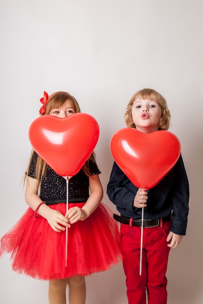 Entzückende Kleinkinder mit Herzen formten den Ballon, der an der Kamera lächelt, die auf Weiß lokalisiert wurde