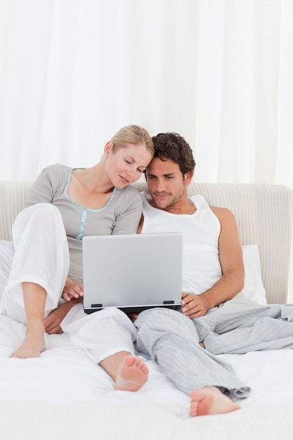 Entzückende Paare, die ihren Laptop auf dem Bett betrachten