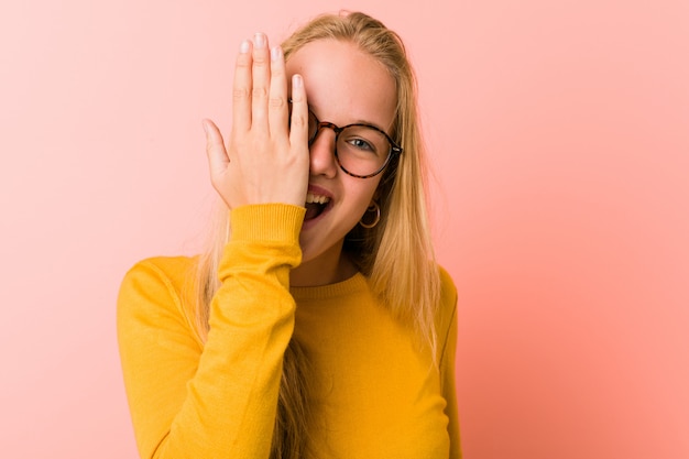 Entzückende Teenagerfrau, die Spaß hat, die Hälfte des Gesichts mit Handfläche bedeckt.