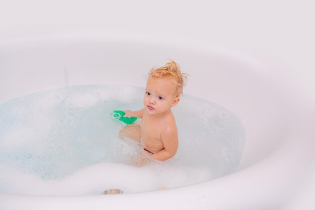 Entzückender blonder Kleinkindjunge, der Spaß mit Wasser hat, indem er in der Badewanne badet Kinderspaßbad