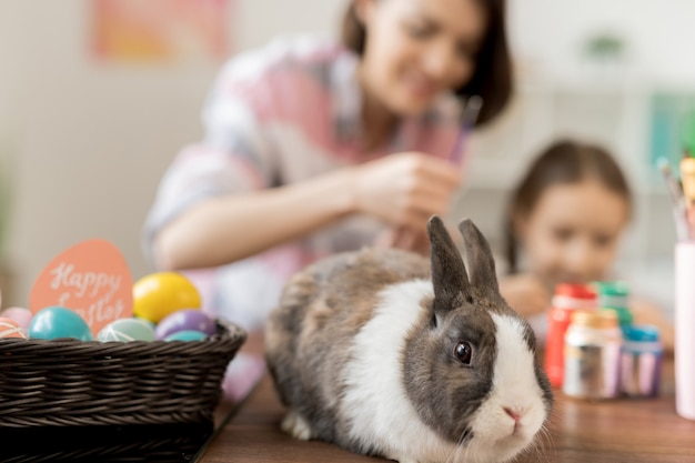 Entzückender Hase und Haufen Ostereier auf Tischmutter- und Tochtermalerei