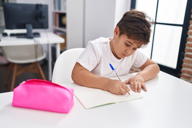 Entzückender hispanischer Junge, der im Klassenzimmer auf Notizbuch schreibt
