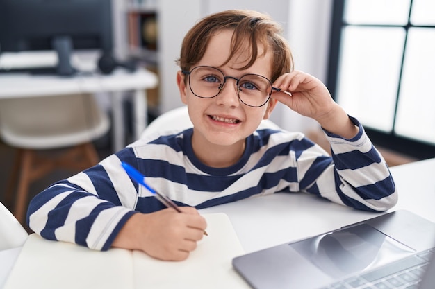 Entzückender hispanischer Junge, der im Klassenzimmer Computerschreiben auf Notizbuch verwendet