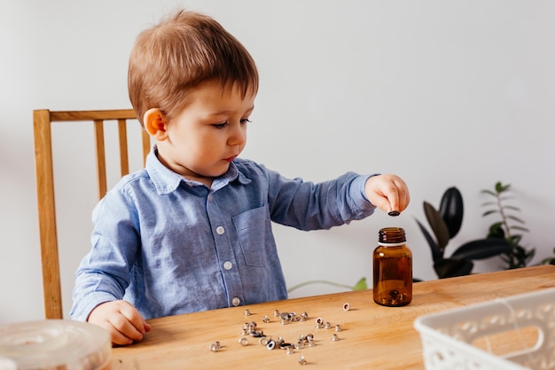 Entzückender Junge füllt Metallknöpfe im Glas