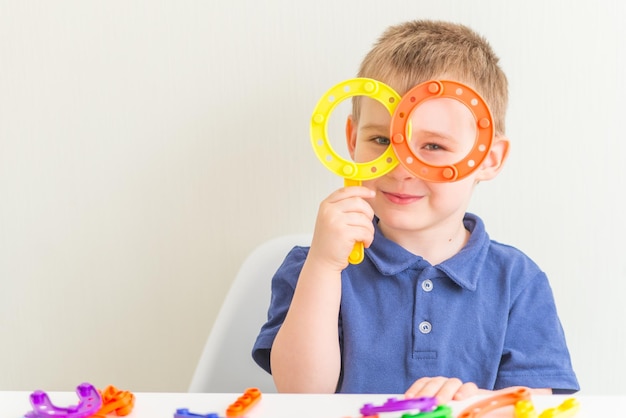Entzückender Junge machte Gläser aus Plastikblockspielzeug und lächelte im Kopierraum horizontales Foto von lustigem Kleinkind