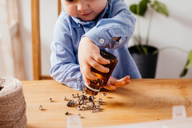 Entzückender Junge streut und füllt Metallknöpfe im Glas