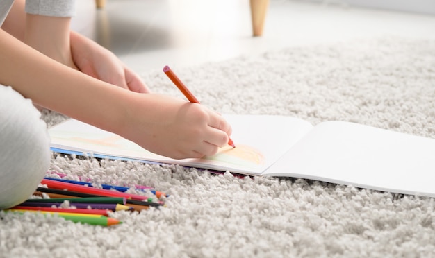 Entzückender kaukasischer Junge im Grundschulalter, der einen Regenbogen mit Bleistiften zeichnet, die zu Hause am Schreibtisch in seinem Zimmer sitzen. Bild mit selektivem Fokus