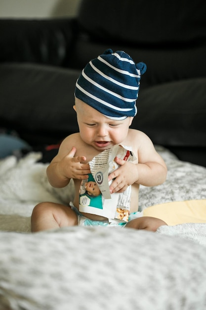 Entzückender kleiner Junge, der im weißen, sonnigen Schlafzimmer krabbeln lernt und mit Papierzeitschriften spielt