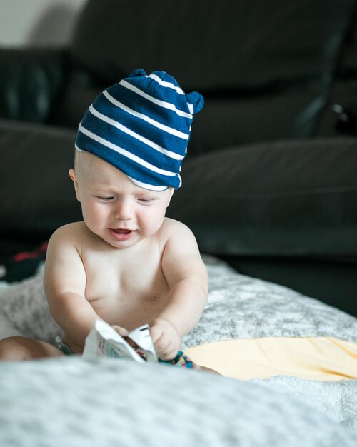 Entzückender kleiner Junge, der im weißen, sonnigen Schlafzimmer krabbeln lernt und mit Papierzeitschriften spielt