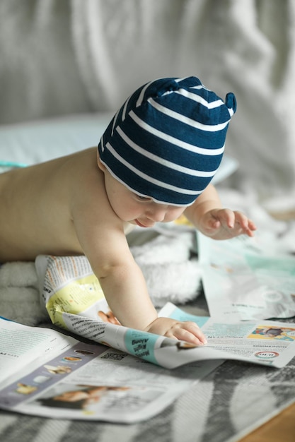 Entzückender kleiner Junge, der im weißen, sonnigen Schlafzimmer krabbeln lernt und mit Papierzeitschriften spielt