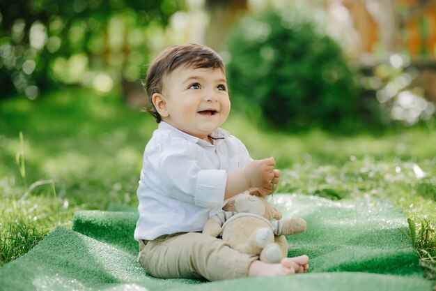 Entzückender kleiner Junge im Garten, der seinen Teddybären lachend hält und Spaß hat