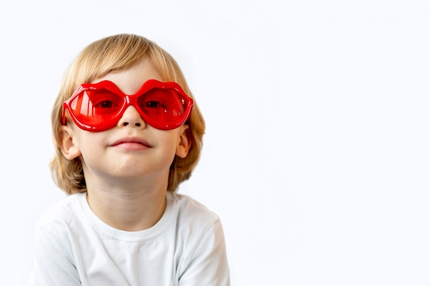 Entzückender lächelnder kleiner Junge im weißen Hemd in der roten Sonnenbrille in Form von Lippen