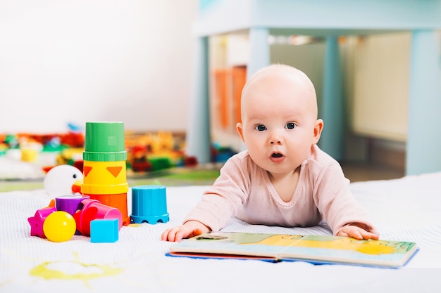 Entzückendes 6 Monate altes Baby, das ein Buch schaut und liest Baby, das zu Hause mit bunten Spielsachen spielt