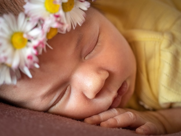 Entzückendes 8 Tage altes neugeborenes Mädchen, das im gelben Strickkleid des Gänseblümchenkranzes auf einem weichen Plaid schläft