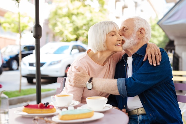 Entzückendes älteres Paar, das Kuss austauscht und im Café sitzt