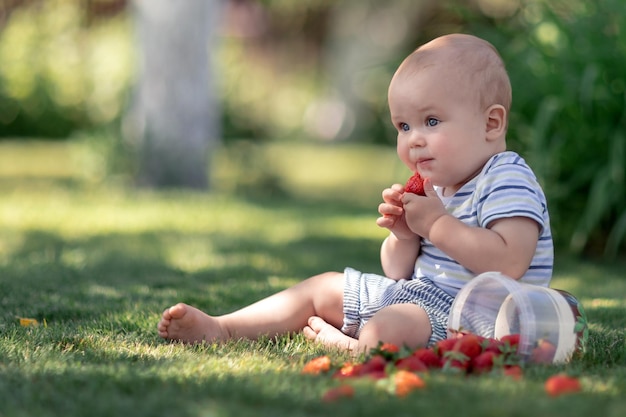 Foto entzückendes baby, das auf dem gras im garten sitzt und erdbeere isst