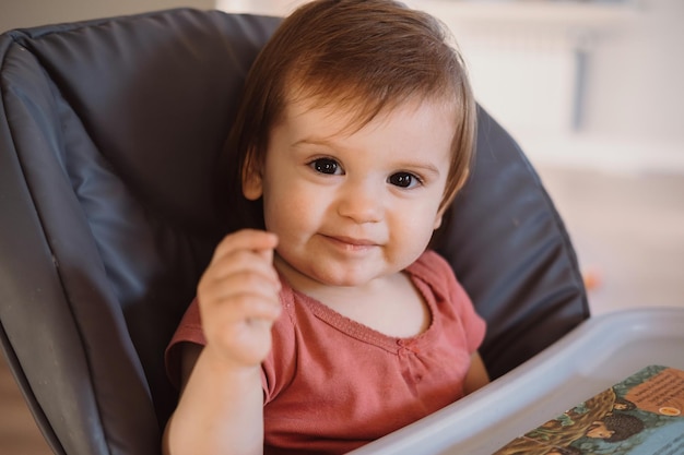 Entzückendes Baby, das auf Essen wartet, während es auf ihrem Hochstuhl sitzt, schöne Mädchen-Babypflege