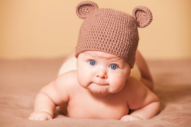 Entzückendes Baby mit Bärenmütze auf dem Bett liegend