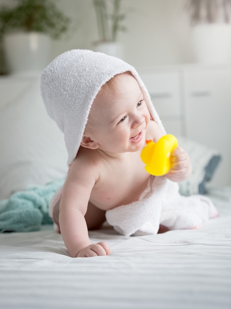 Entzückendes Baby mit einem Handtuch bedeckt, das eine gelbe Gummiente hält