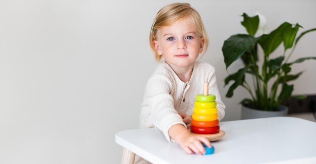 Entzückendes blondes Kleinkind Kind Mädchen zwei Jahre alt, das drinnen mit Öko-Holzspielzeug Pyramidion auf weißgrauem Hintergrund spielt Platz kopierenFrühe Vorschulentwicklung Kindergartenspiel