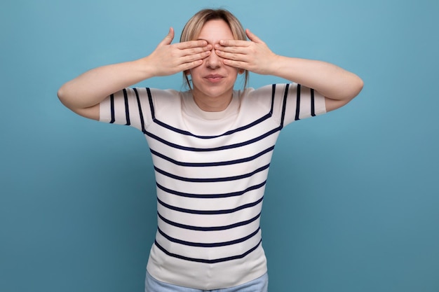 Entzückendes blondes Mädchen schloss die Augen mit den Händen auf einem blauen Hintergrund mit Kopierraum