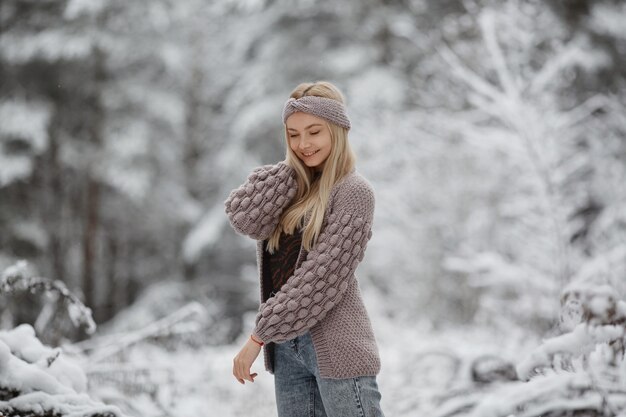 Entzückendes blondes Model-Mädchen mit langen Haaren, das eine gestrickte gemütliche Strickjacke trägt, posiert draußen auf einem frostigen...