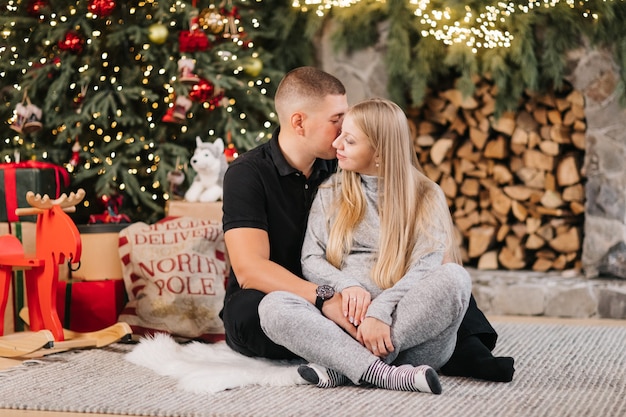 Entzückendes Ehepaar sitzt in der Nähe von Weihnachtsbaum und Kamin zu Hause