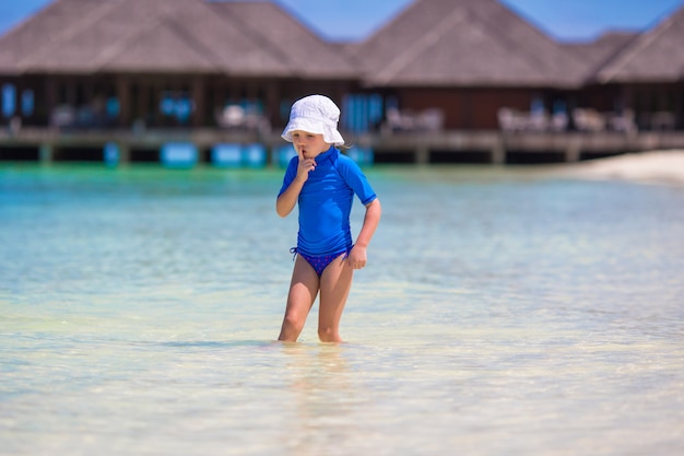 Entzückendes glückliches kleines Mädchen, das am seichten Wasser an den tropischen Ferien spielt