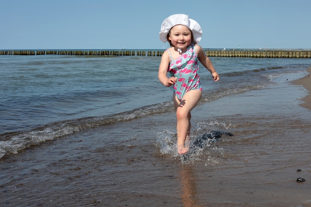 Entzückendes glückliches lächelndes kleines Mädchen im Strandurlaub, das entlang der Küste läuft