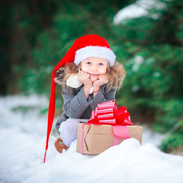 Entzückendes glückliches Mädchen mit Weihnachtsgeschenk im Winter draußen auf Weihnachtsabend