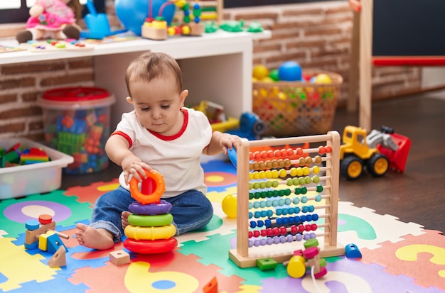 Entzückendes hispanisches Baby, das im Kindergarten auf dem Boden sitzt und mit Abakus und Reifen spielt