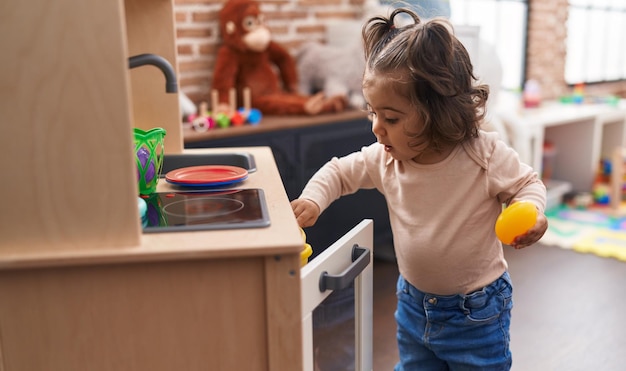 Entzückendes hispanisches Mädchen, das mit der Spielküche spielt, die im Kindergarten steht