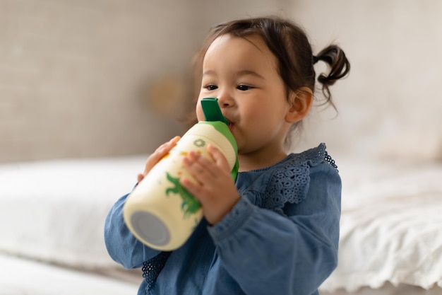 Entzückendes japanisches Mädchen trinkt Wasser aus der Flasche im Schlafzimmer