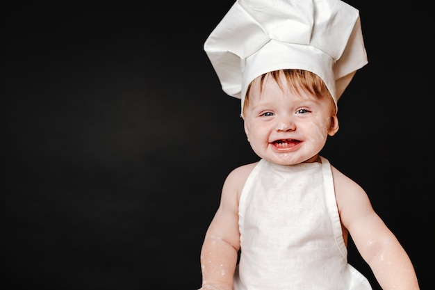 Entzückendes Kind im Hut des Kochs und der Schürze