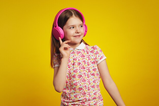 Entzückendes Kind in stilvoller Sommerkleidung, das Musik über Kopfhörer hört