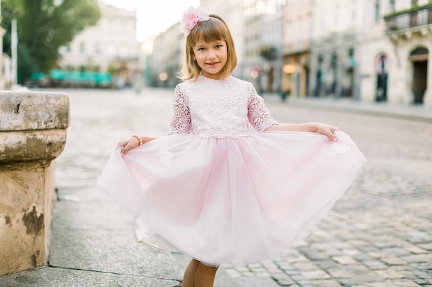 Foto entzückendes kleines blondes mädchen in einem rosa kleid in der stadt