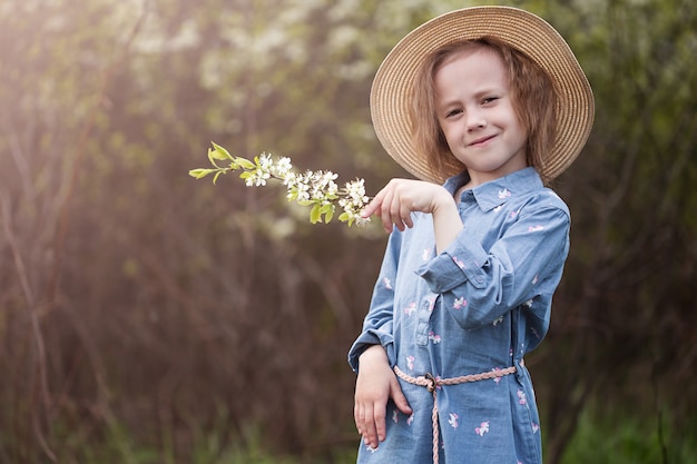 Entzückendes kleines kaukasisches Mädchen 5 Jahre alt in einem Hut im Park, der unter den Kirschblüten mit selektivem Fokus und unscharfem Hintergrund steht