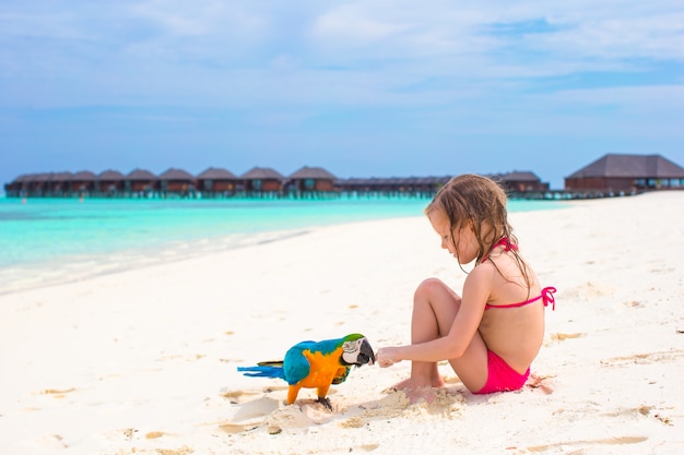 Entzückendes kleines Mädchen am Strand mit buntem Papagei