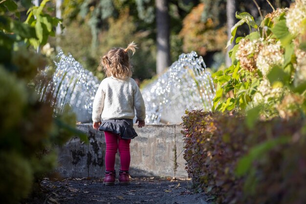 Entzückendes kleines Mädchen betrachtet das Brunnenkleinkind in einem Park mit Brunnen an einem sonnigen Tag Familie