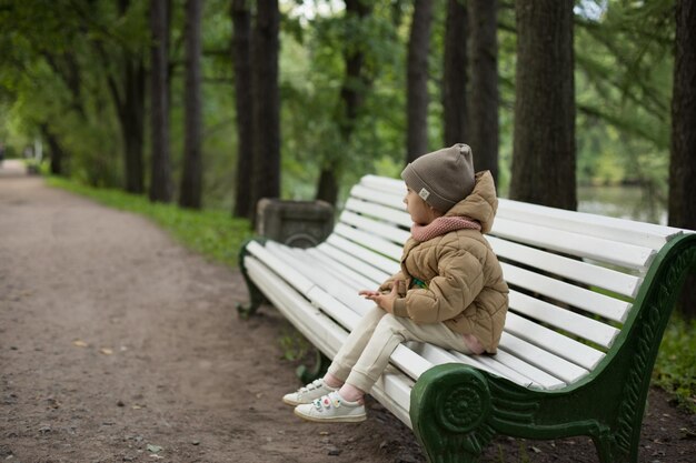 Entzückendes kleines Mädchen, das an einem sonnigen Herbsttag auf einer Bank im Herbstpark sitzt Fröhliches Kind, das Spaß im Freien hat Outdoor-Herbstaktivitäten für Kinder