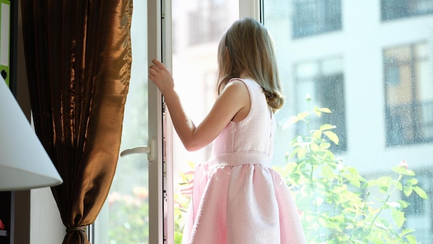 Entzückendes kleines Mädchen, das an einer großen Glastür oder einem Fenster steht
