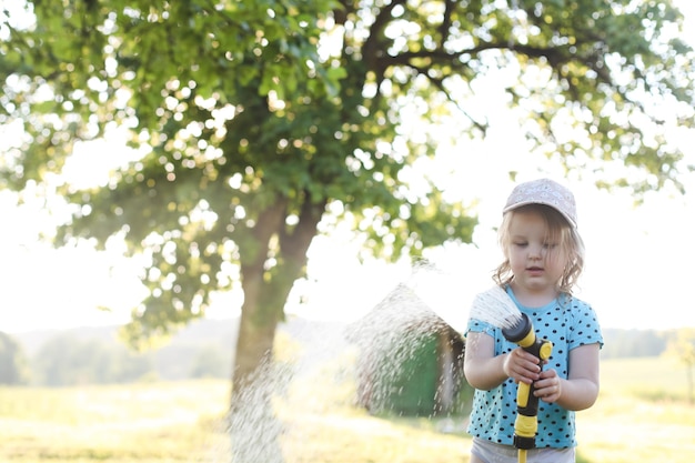 Entzückendes kleines Mädchen, das an heißen und sonnigen Sommertagen mit einem Gartenschlauch spielt